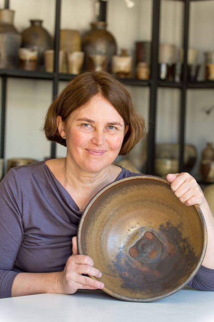 Ceramic artist Beatričė Kelerienė holding a wood-fired ceramic work in her studio